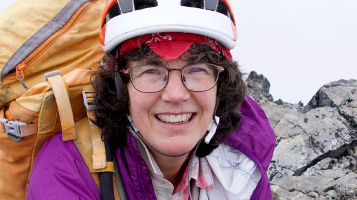 Nelson, wearing hiking gear, smiles at the camera at the top of a rocky outcrop.