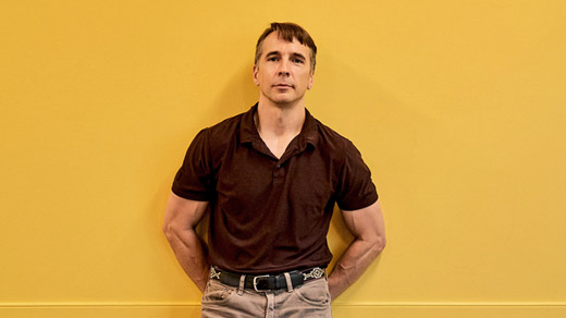 Richard Rusczyk standing in front of a yellow wall in an Art of Problem Solving classroom in San Diego.