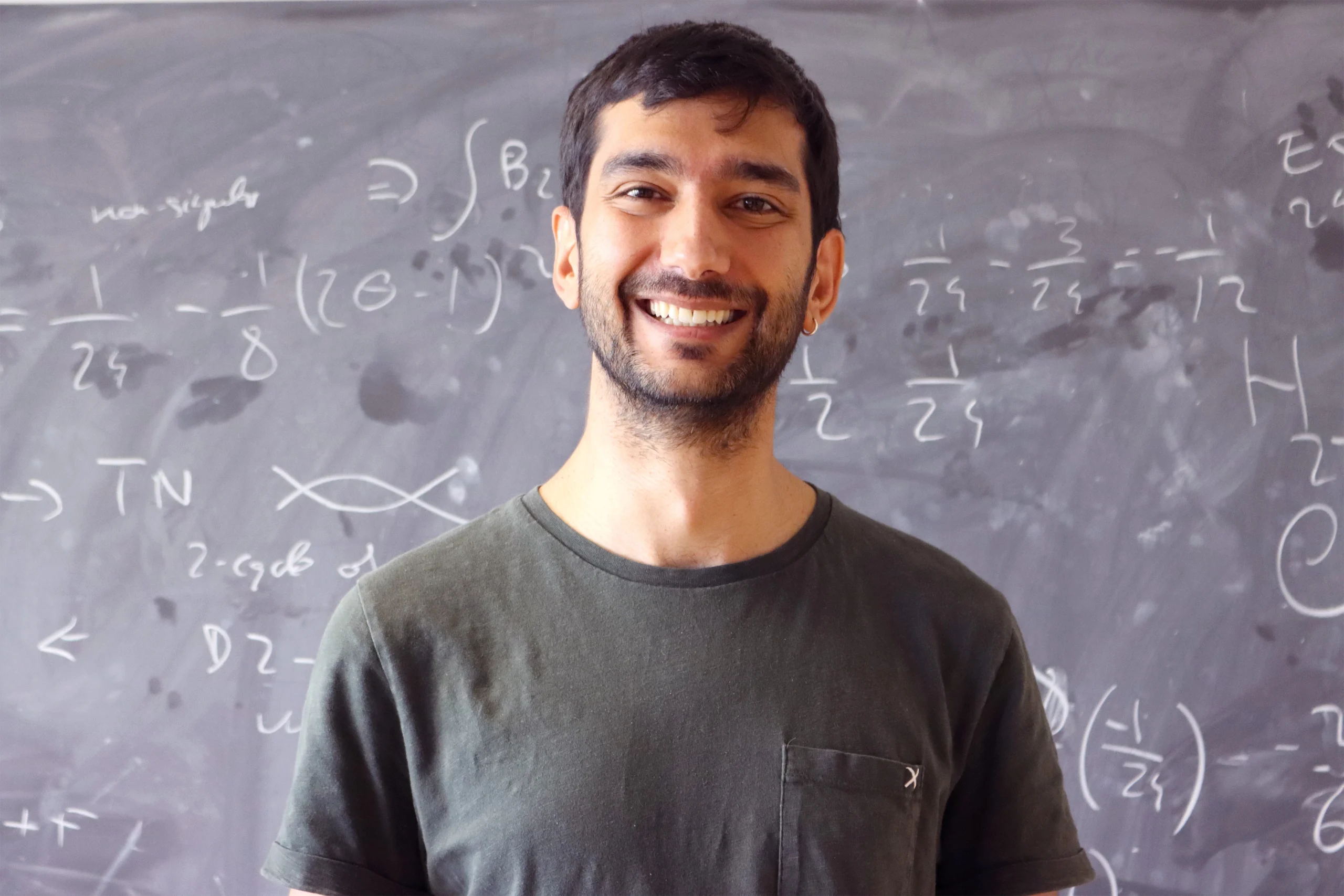 Álvaro Alhambra in a green shirt stands in front of a chalkboard with figures on it