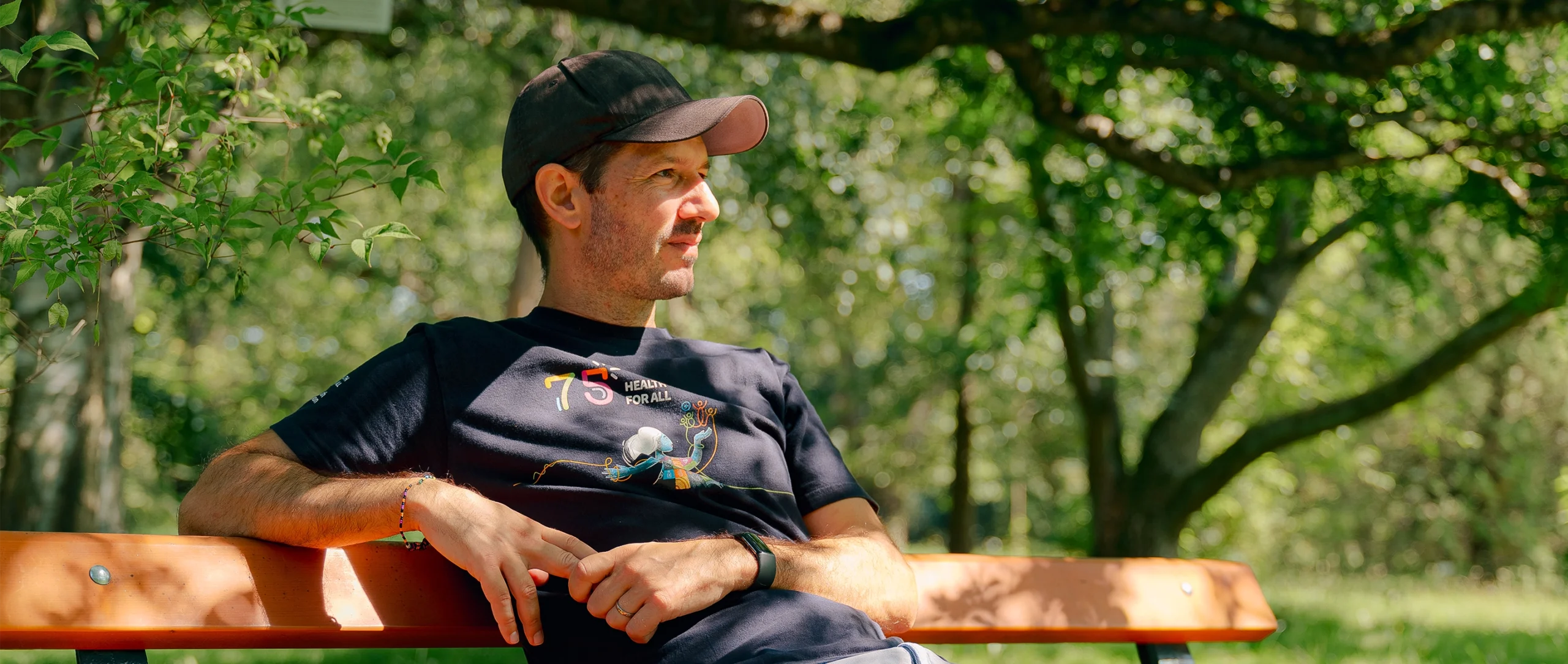 Sébastien Calvignac-Spencer sits on a park bench wearing a T-shirt and baseball cap.