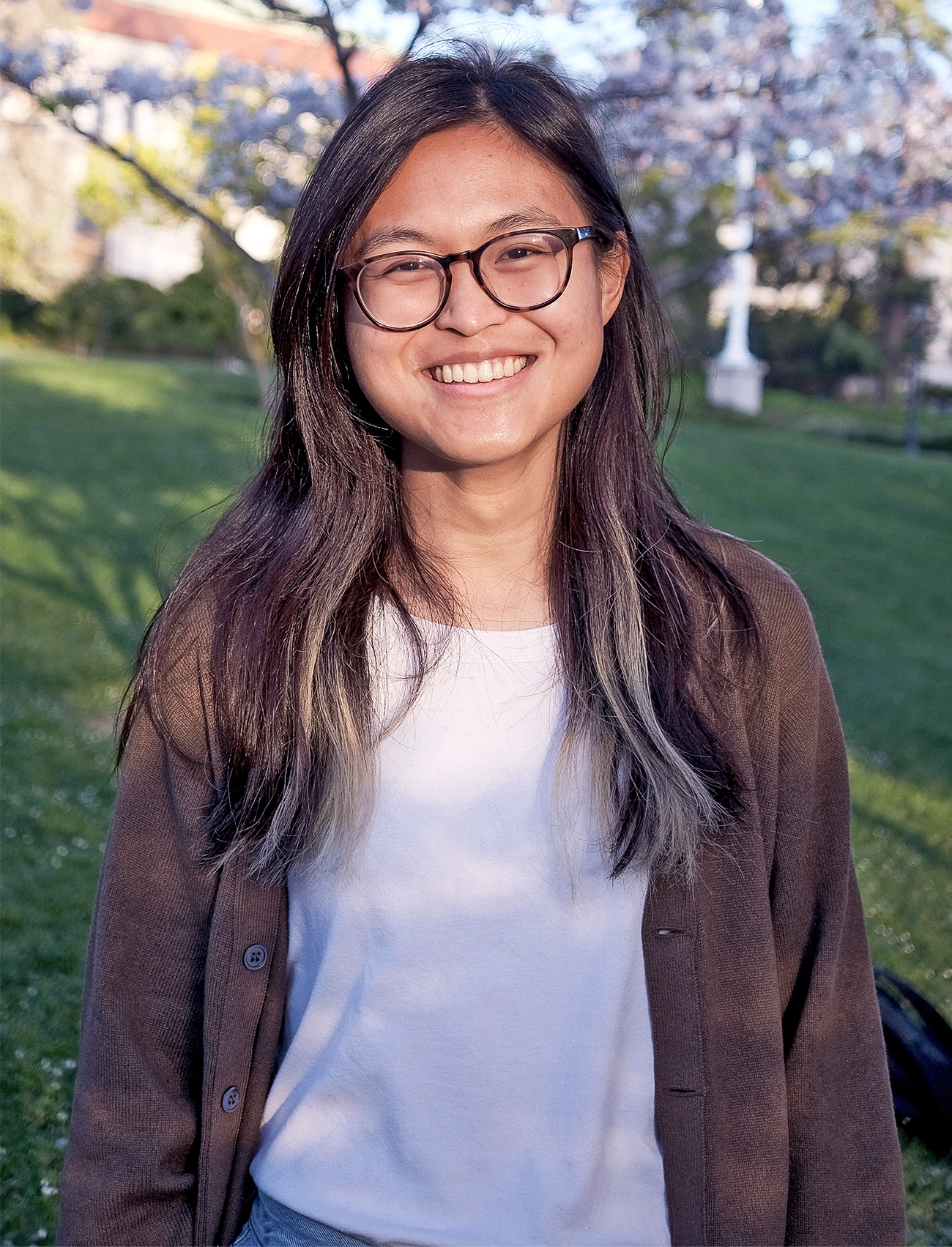 Ewin Tang in a white shirt and brown sweater stands outside