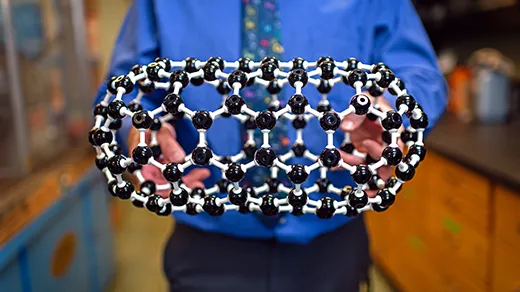 Hands hold a ball-and-stick model of a pill-shaped molecule called a fullertube.