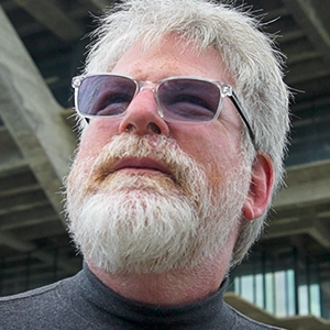 Russel Impagliazzo wearing a dark shirt and sunglasses stands outside a tree-shaped building